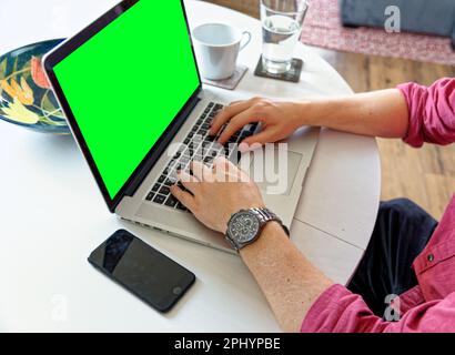 Young professional man using a laptop with a green screen - wearing a fashion watch. Work from home - London, United Kingdom, 1st of June 2019 Stock Photo