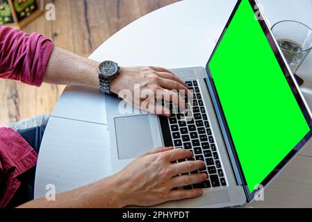 Young professional man using a laptop with a green screen - wearing a fashion watch. Work from home - London, United Kingdom, 1st of June 2019 Stock Photo