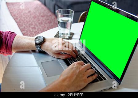 Young professional man using a laptop with a green screen - wearing a fashion watch. Work from home - London, United Kingdom, 1st of June 2019 Stock Photo