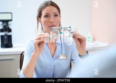 Optometrist is holding trial frame in hands while sitting in the modern clinic Stock Photo
