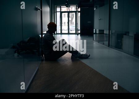 Despondent corporate worker seated in office corridor Stock Photo