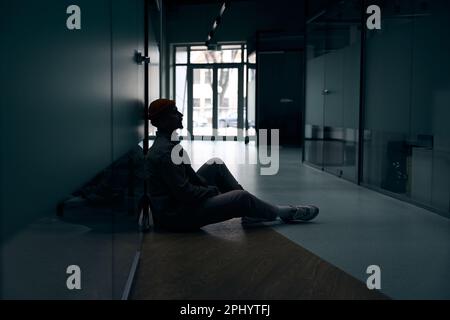 Depressed company employee seated alone in dark corridor Stock Photo