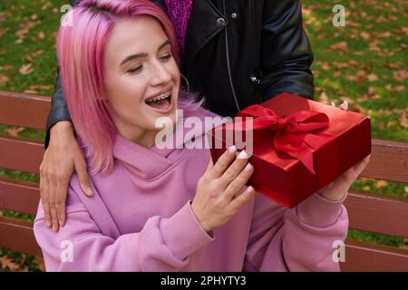 Happy lady receiving present from female companion outdoors Stock Photo