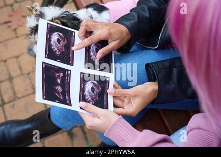 Female showing ultrasound images of unborn baby to female companion Stock Photo