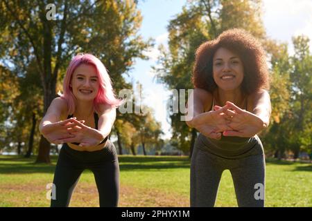 Joyful sporty ladies doing stretching exercise outdoors Stock Photo