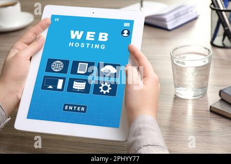Web hosting service. Woman with modern tablet at wooden table in office, closeup Stock Photo