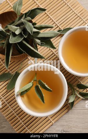 Aromatic sage tea and fresh leaves on table, flat lay Stock Photo
