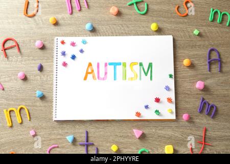 Flat lay composition of notebook with word Autism and plasticine on wooden table Stock Photo