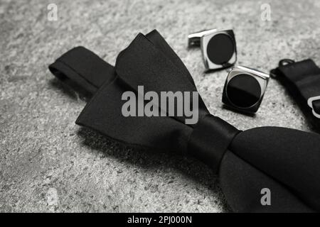Stylish black bow tie and cufflinks on grey stone background, closeup Stock Photo