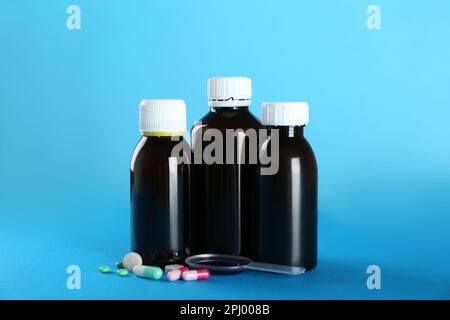 Bottles of cough syrup, dosing spoon and pills on light blue background Stock Photo