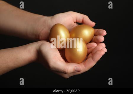 Woman holding shiny golden eggs on black background, closeup Stock Photo