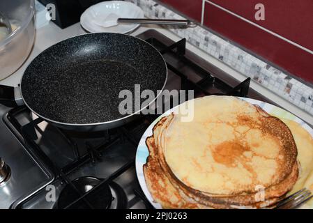 Plate of freshly made crepes and frying pan on stove in kitchen Stock Photo
