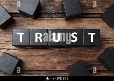 Word TRUST made with black cubes on wooden table, flat lay Stock Photo