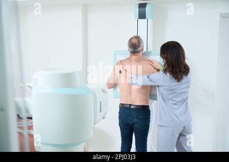 Professional radiologist helping male patient with the X-ray machine in a clinic Stock Photo
