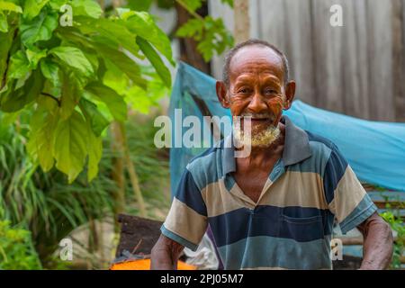 Raja Ampat, Indonesia -February 6. 2023: Old man with beard sitting on wood and looking in the camera in West Papua, close up Stock Photo