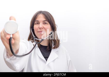 Close-up Front view of a young female doctor showing stethoscope smiling with white background Stock Photo