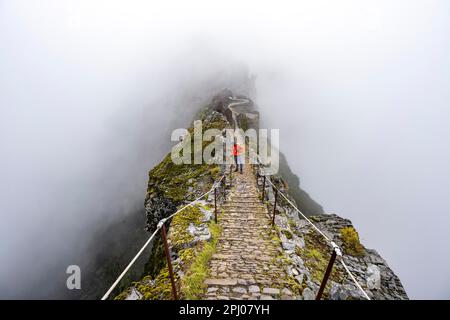 Hikers in the mist, Pico Arieiro to Pico Ruivo hike, narrow exposed trail on rocky cliff, Central Mountains of Madeira, Madeira, Portugal Stock Photo