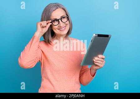 Photo of clever dreamy lady dressed coral shirt arm eyewear reading modern device looking empty space isolated blue color background Stock Photo