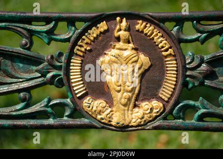 Gold colour motif made of metal depicting a Buddha riding an elephant on a bench seat in Lumphini Park, Bangkok, Thailand. Stock Photo