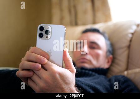 a man lying on a bed looking at new phone iPhone 13 Pro Max great choice ordinary person Real life everyone can afford Great photo of a hand close-up blurry face Ukraine 2023 Stock Photo