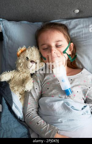 Sick little girl having medical inhalation treatment with nebuliser. Child with breathing mask on her face lying in bed Stock Photo