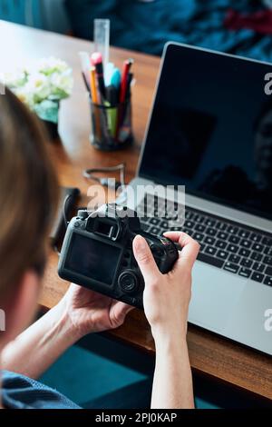 Female photographer working on photos on laptop and camera. Woman editing retouching browsing photos working as a freelancer sitting at desk Stock Photo