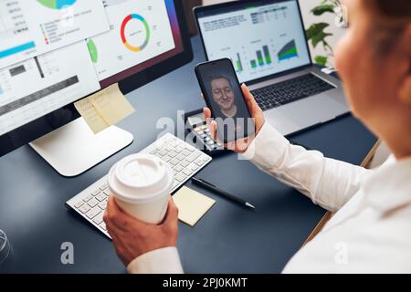 Woman entrepreneur having business video chat on smartphone. Businesswoman working with data on charts, graphs and diagrams on computer screen. Woman Stock Photo