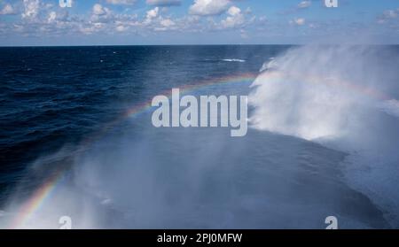 Rainbow formed by sunlight shining on the waves formed by the boat moving through the sea, on a bright sunny day traveling on the ocean Stock Photo