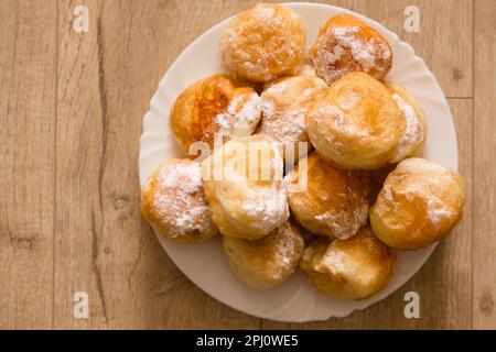 Ruddy fragrant donuts sprinkled with powdered sugar in a plate on a wooden background Stock Photo