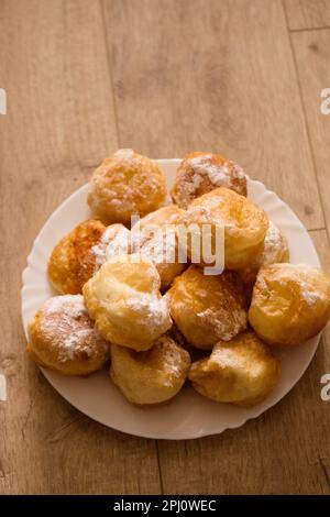 Ruddy fragrant donuts sprinkled with powdered sugar in a plate on a wooden background Stock Photo