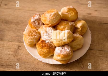 Ruddy fragrant donuts sprinkled with powdered sugar in a plate on a wooden background Stock Photo