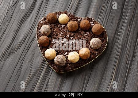 White, milk and dark chocolate truffles and chocolate chips in a heart-shaped box on a dark wooden background, top view. Valentine's Day. Stock Photo