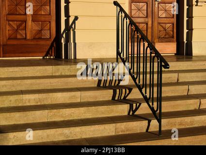 wide exterior stone stairs. deep treads and defined vertical risers. decorative painted black wrought iron railing. elegant stained oak entrance door. Stock Photo