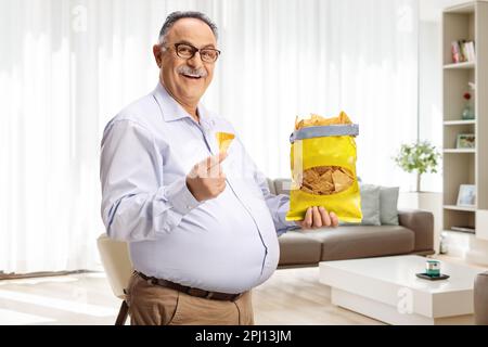 Cheerful mature man eating tortilla chips and smiling at home Stock Photo
