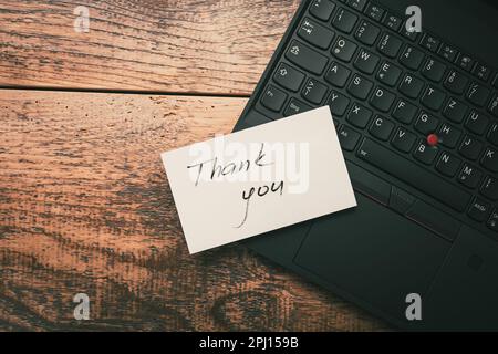 Closeup of Thank You sticky note message on laptop on wooden background Stock Photo