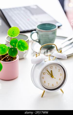 Time management and procrastination concept. Composition with alarm clock on white desk, laptop computer, coffee and plant Stock Photo