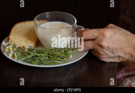 https://l450v.alamy.com/450v/2pj18pg/old-hand-holds-a-cup-of-milk-near-daisies-and-a-piece-of-bread-at-a-table-2pj18pg.jpg
