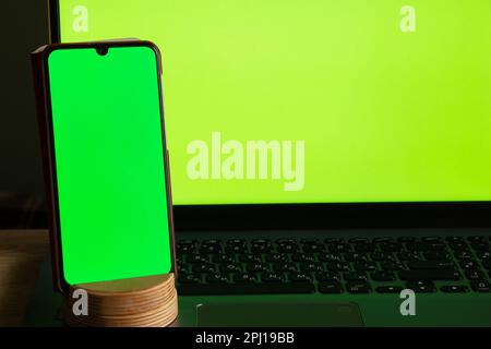 a laptop with a green screen and a touch phone is on the table Stock Photo