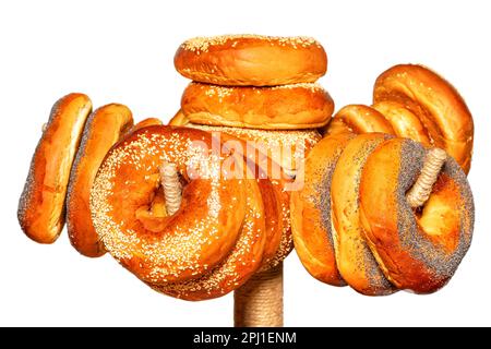 Appetizing bagels are topped with sesame seeds and poppy seeds hanging on a rack. Isolated on white Background. Selective focus. Stock Photo
