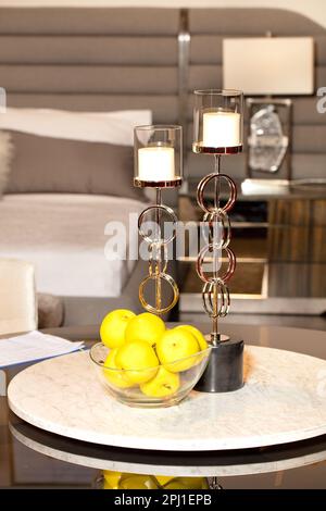 Bedroom interior design, graceful candlestick, vase with yellow apples on marble coffee table against bedroom background in blur. Vertical image. Stock Photo