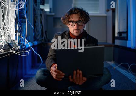 A system administrator working in server room using laptop Stock Photo