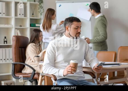 Handsome businessman with cup of coffee using mobile phone in office Stock Photo