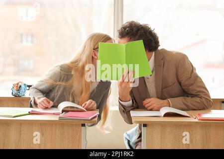 Teenage couple covering themselves with copybook in classroom Stock Photo