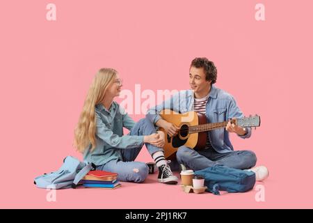 Teenage girl with her boyfriend playing guitar on pink background Stock Photo