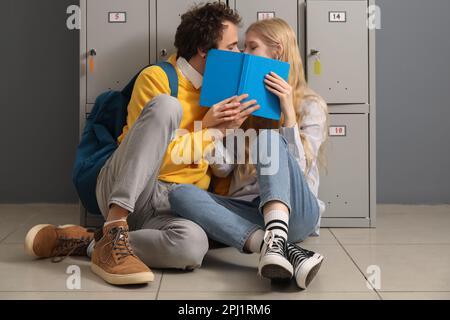 Cute teenage couple covering themselves with book near locker at school Stock Photo