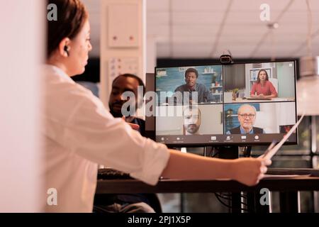 Corporate team online briefing, report presentation discussion on videocall meeting, woman attending online videoconference on computer. Coworkers teleconference in coworking space at night Stock Photo