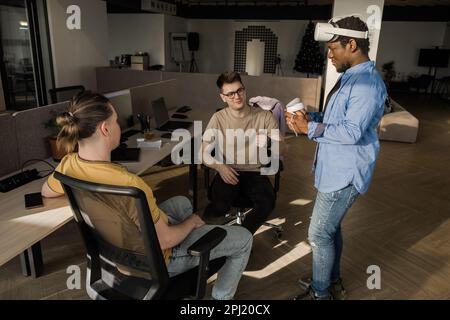 IT Development Team Working on VR Project. Man wearing VR headset, playing and touching something in the virtual world. Diverse men programmers using Stock Photo