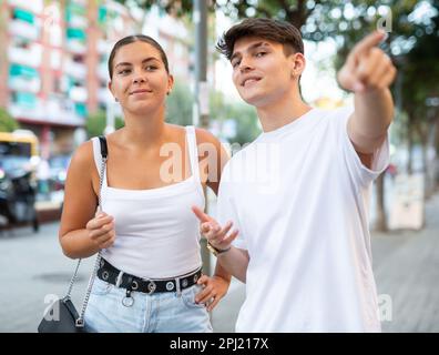 Happy young couple pointing while looking at something on city street Stock Photo