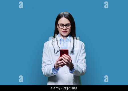 Young woman doctor using smartphone on blue background Stock Photo