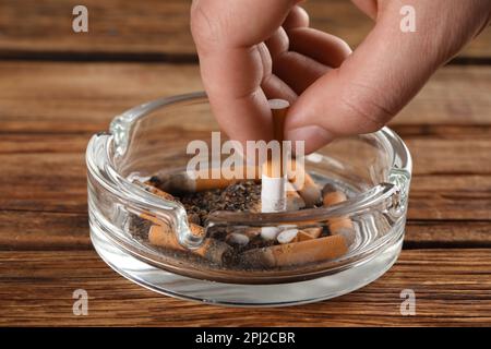 Man putting out cigarette in ashtray on wooden table, closeup Stock Photo